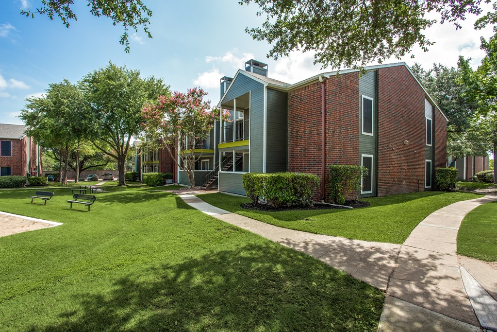 a brick building with green grass and trees and a sidewalk