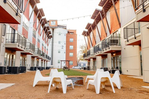 A courtyard with white chairs and tables is surrounded by apartment buildings.