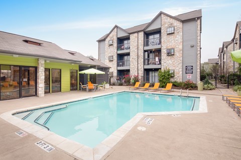A pool surrounded by chairs and umbrellas in front of a building.
