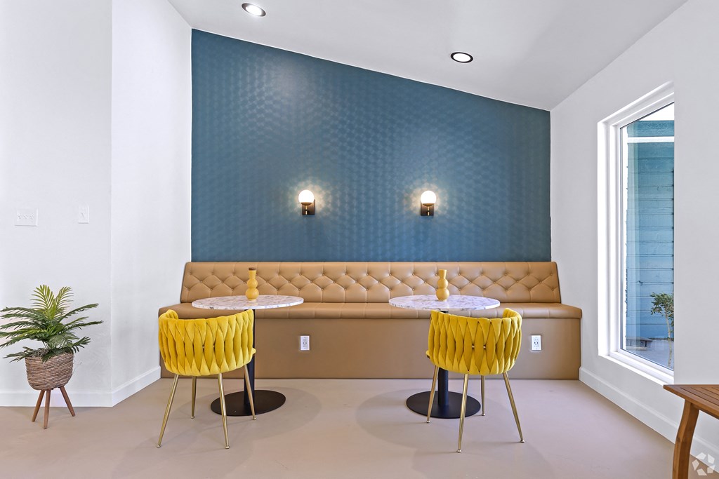 a seating area with two tables and two yellow chairs in front of a blue wall with three