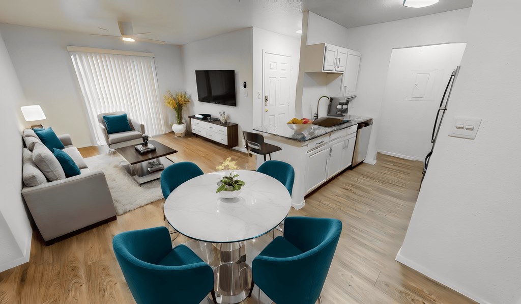 Modern open-plan living room and kitchen in an east riverside apartment with stylish decor, including a round table with teal chairs, beige sofa, and wooden flooring.