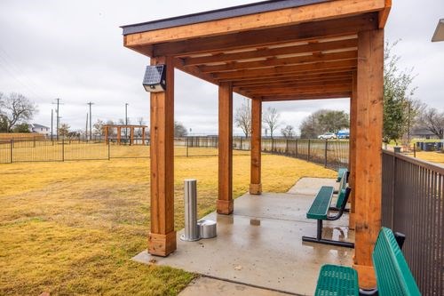 A wooden shelter with a solar panel on top is situated in a grassy area with benches at Lockhart Farms Apartments, Texas