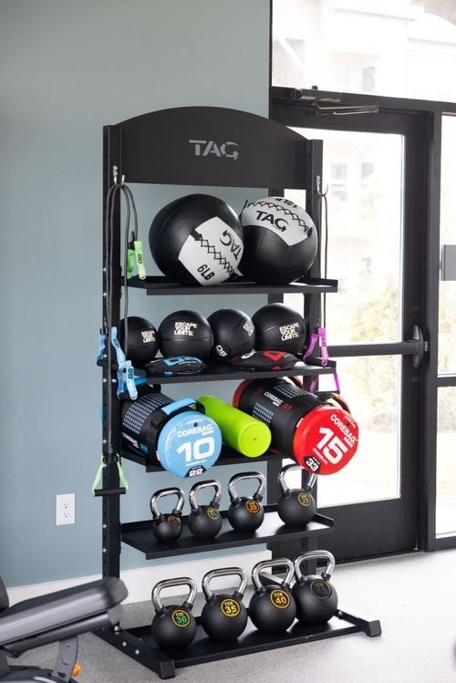 A black shelf with a variety of fitness equipment including kettlebells and a jump rope at Lockhart Farms Apartments, Lockhart 78644