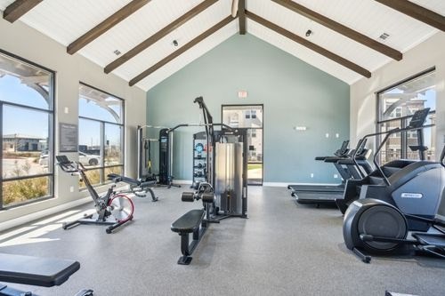 A spacious gym with a variety of equipment including treadmills, stationary bikes, and weight machines at Lockhart Farms Apartments, Lockhart