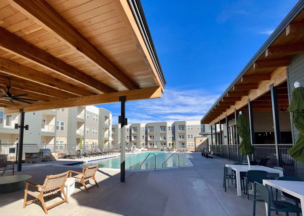 A wooden patio with chairs and a table overlooking a pool at Lockhart Farms Apartments, Lockhart, TX, 78644