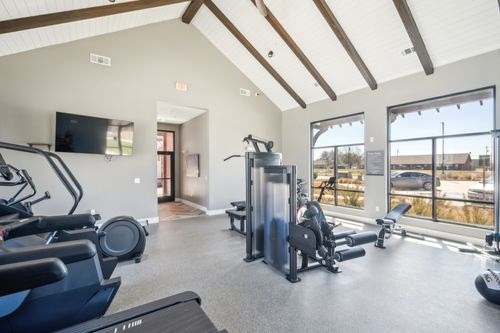 A gym with treadmills, elliptical machines, and a television at Lockhart Farms Apartments, Lockhart, Texas