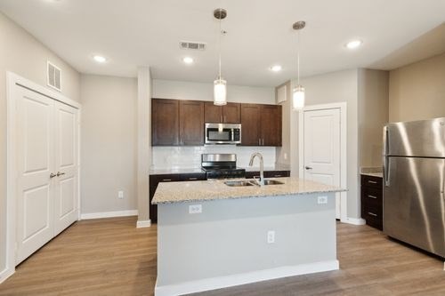 A kitchen with a stainless steel refrigerator and a granite countertop at Lockhart Farms Apartments, Lockhart, Texas