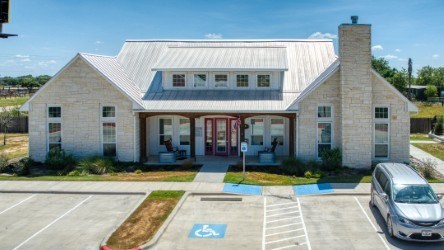 A white building with a red door and a parking lot in front.