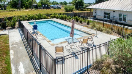 A pool surrounded by a black fence with a sun lounger and table.