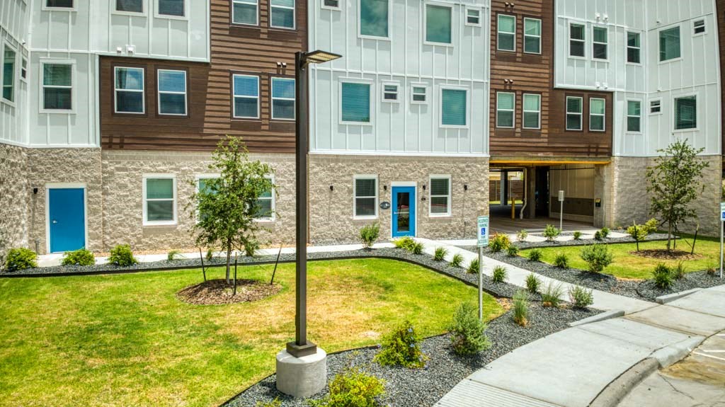 an exterior view of an apartment building with a yard and sidewalk