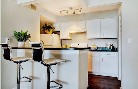 A kitchen with white cabinets and a bar area with two stools.