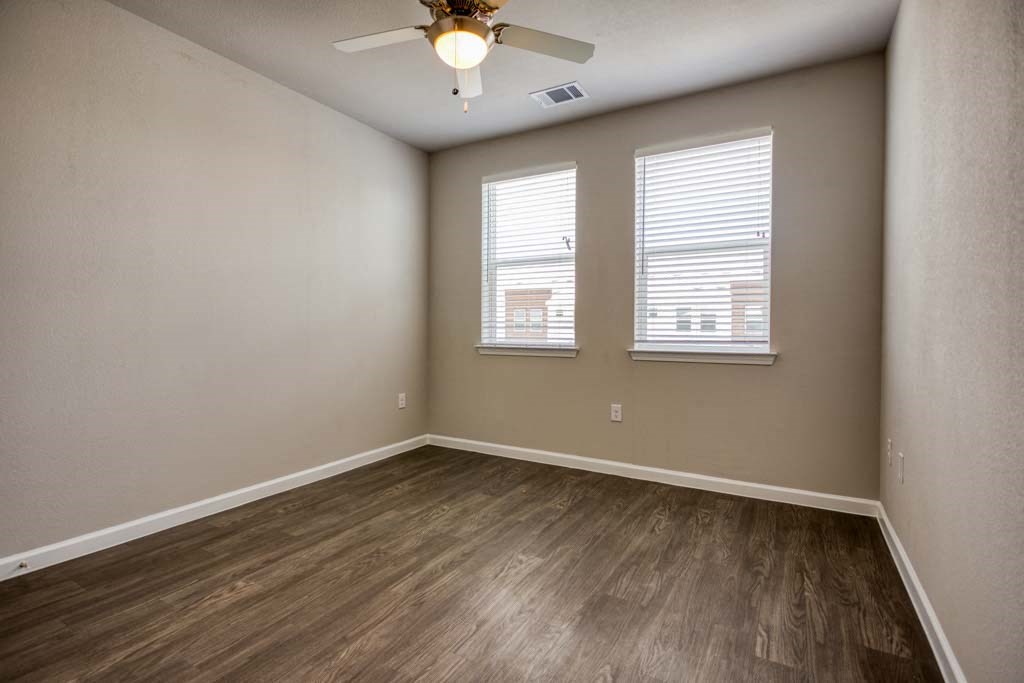 an empty room with a ceiling fan and three windows