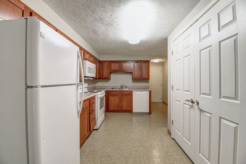 A kitchen with a white refrigerator and brown cabinets.