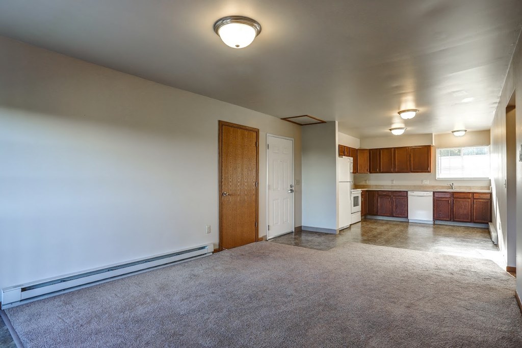 an empty living room with a kitchen in the background