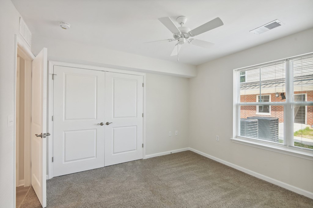 an empty bedroom with a ceiling fan and a window
