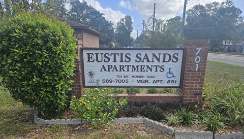 A sign for Eustis Sands Apartments is displayed in front of a building.