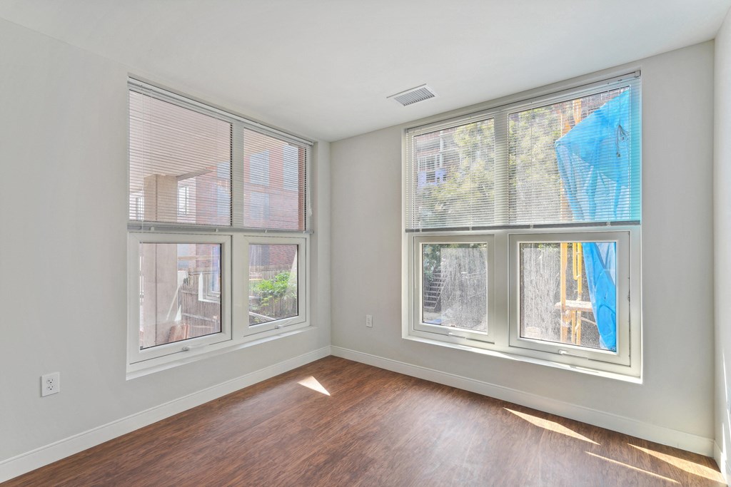 a bedroom with three large windows and hardwood floors