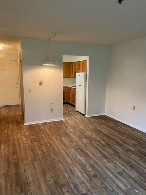 A room with wooden flooring and a white refrigerator.