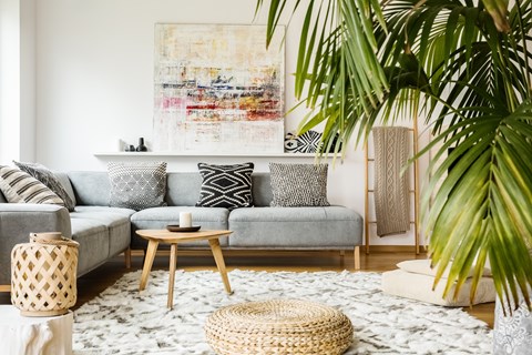 A living room with a grey couch, a woven stool, and a large abstract painting on the wall.