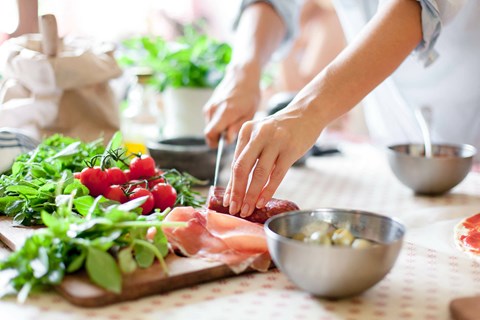 a woman cutting meat on a cutting board with vegetables on a table
