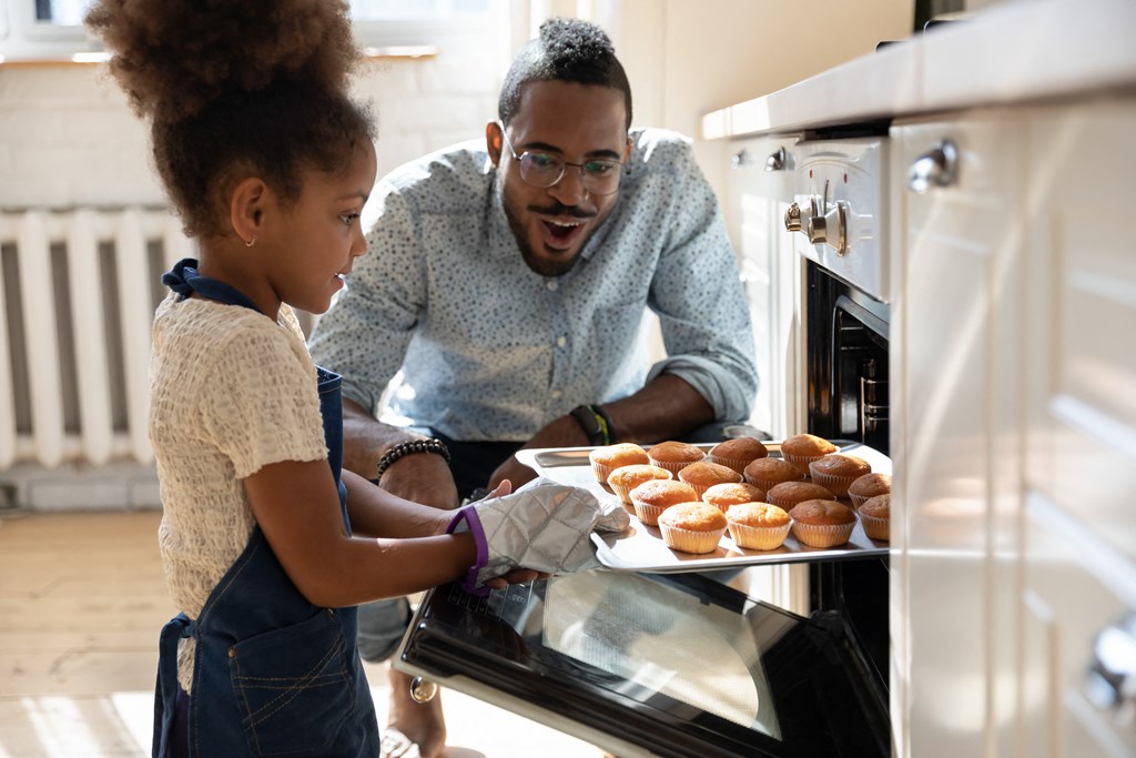 a father and daughter putting a tray of donuts into an oven