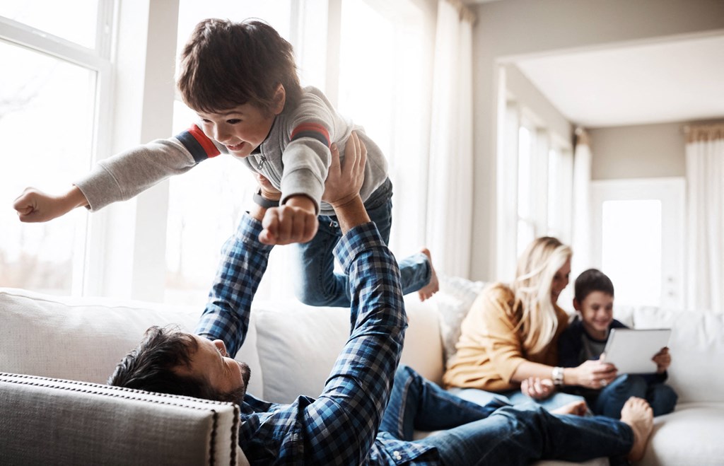 a young boy jumping on a man in the living room with his family