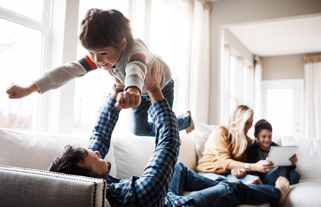 a young boy jumping on a man in the living room with his family