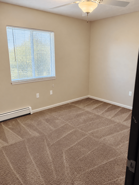 A room with a carpeted floor and a window with blinds.