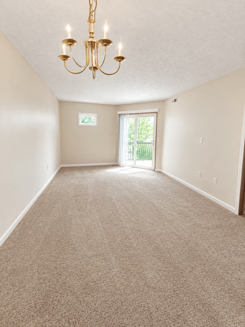 A room with a carpet floor and a chandelier hanging from the ceiling.