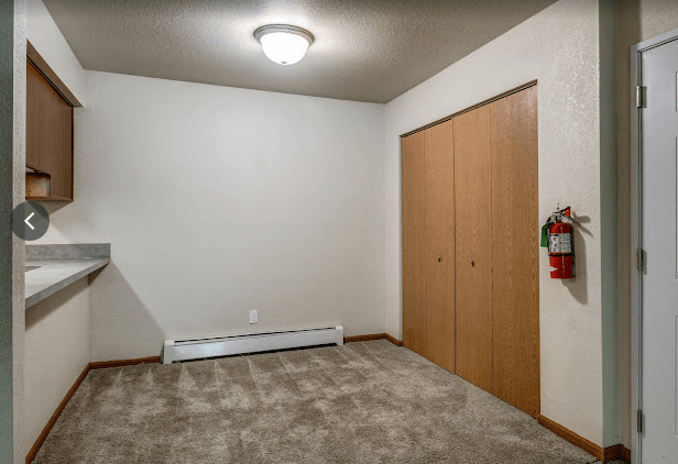 an empty room with a carpeted floor and a door to a kitchen