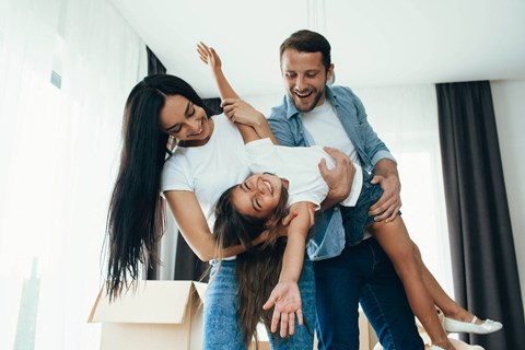 two women and a man holding a child in a room with boxes