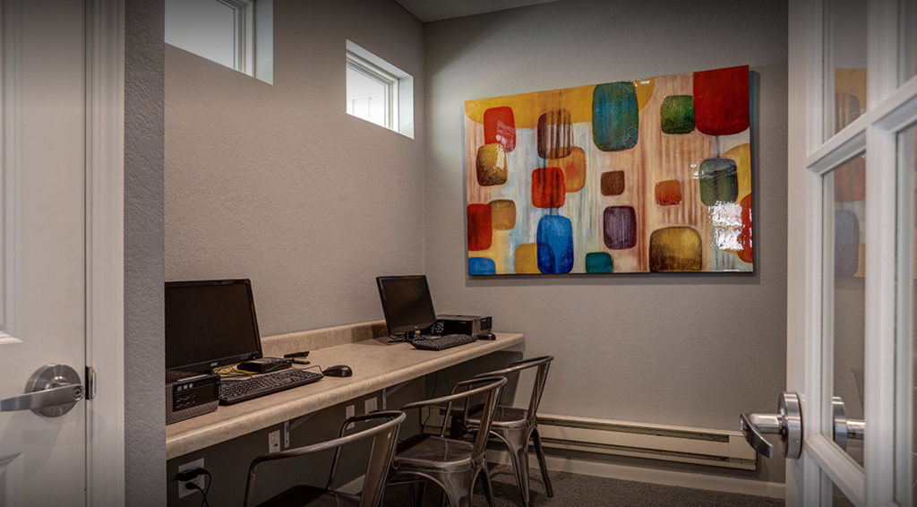 a study room with two computers and a painting on the wall