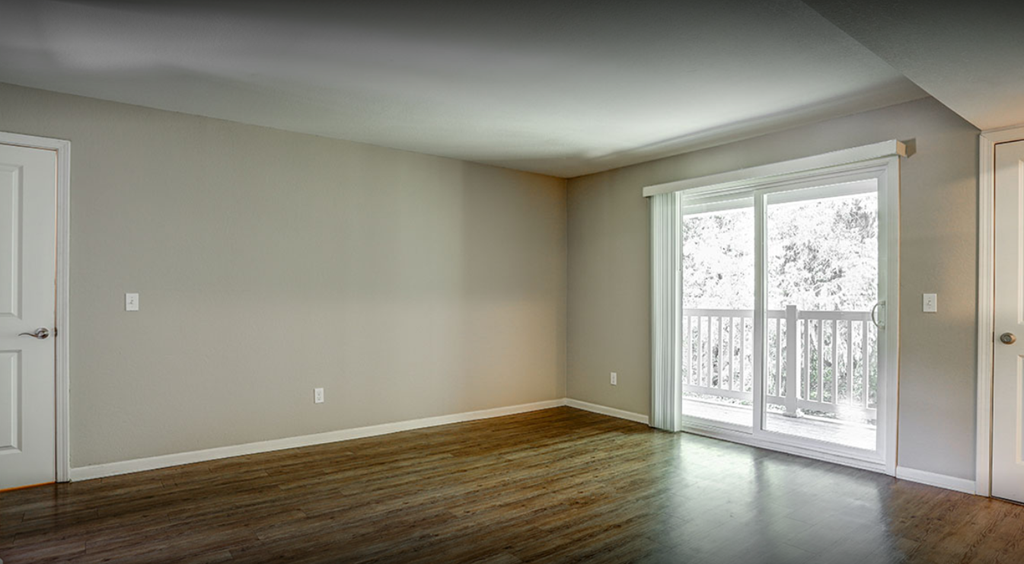 an empty living room with wood floors and a door to a balcony