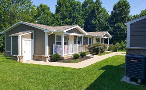 a small gray house with a porch and a yard with a lawn and trees