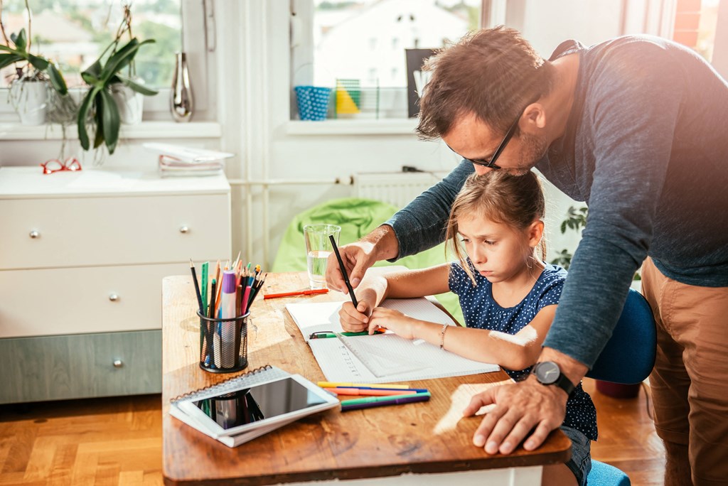a father helping his daughter draw on a piece of paper at a desk