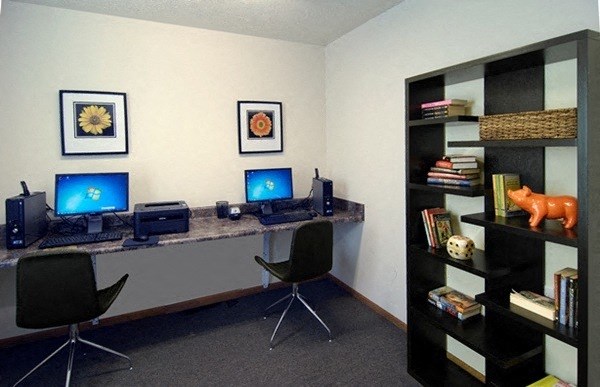 an office with a desk with two computers and a bookshelf