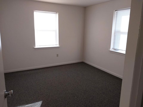 A room with a carpeted floor and two windows.