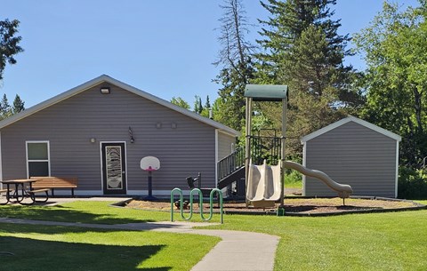 A playground with a slide, swings, and a picnic table is located in front of a building.