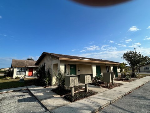 A house with a red door and a green door is surrounded by plants and a sidewalk.