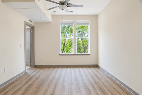 A room with a ceiling fan and a window overlooking trees.
