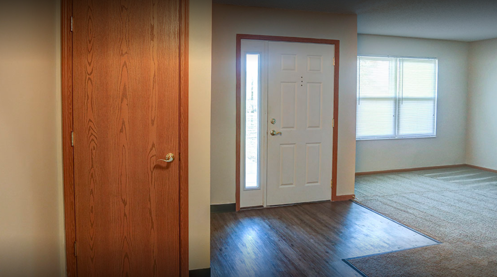 an empty living room with a white door and wood floors