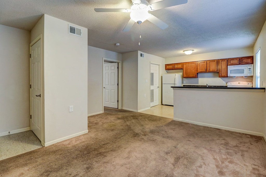 an empty living room with a kitchen and a ceiling fan