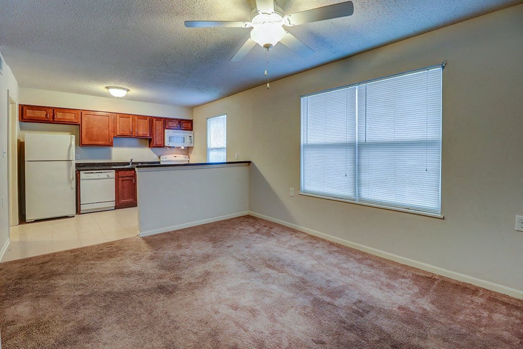 an empty living room with a kitchen and a ceiling fan