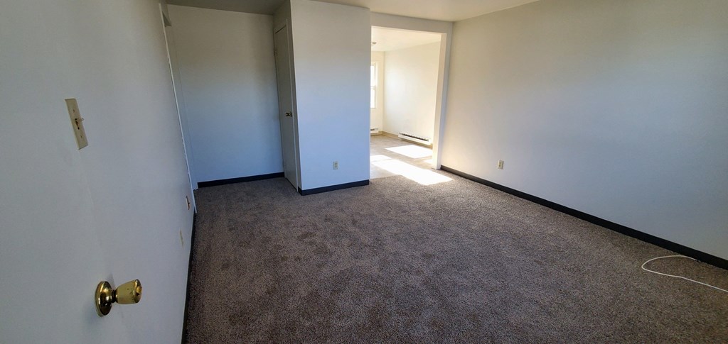a room with a carpeted floor and white walls and a door to a hallway