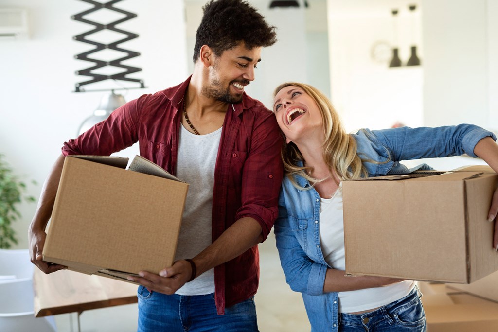 a couple laughing while holding boxes in a room