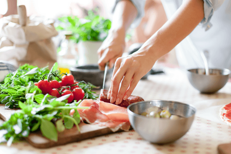 a woman cutting meat on a cutting board with vegetables