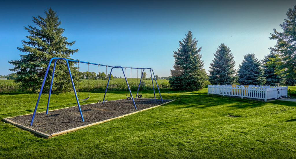 a swing set in the grass with trees and a fence