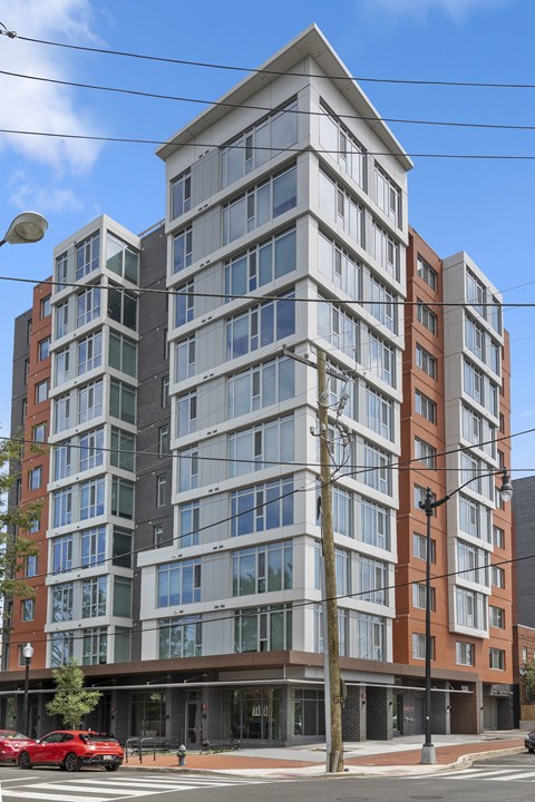 A modern multi-story building with a red car parked in front.