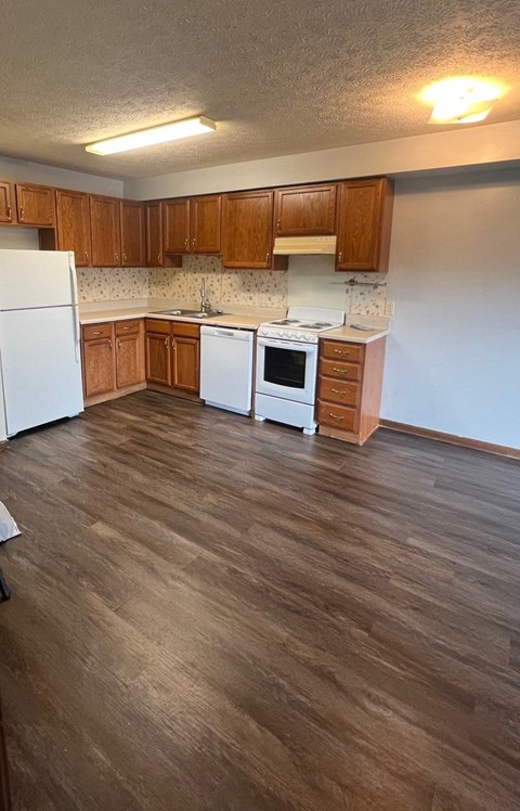an empty kitchen with wooden floors and white appliances