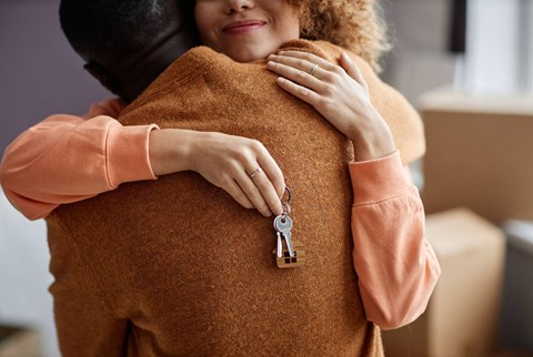 A person in a brown sweater is hugging another person and has a key hanging from their sweater.